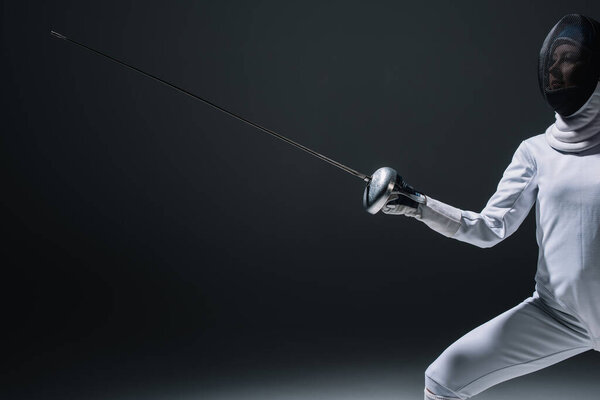 Cropped view of fencer in fencing mask holding rapier on black background