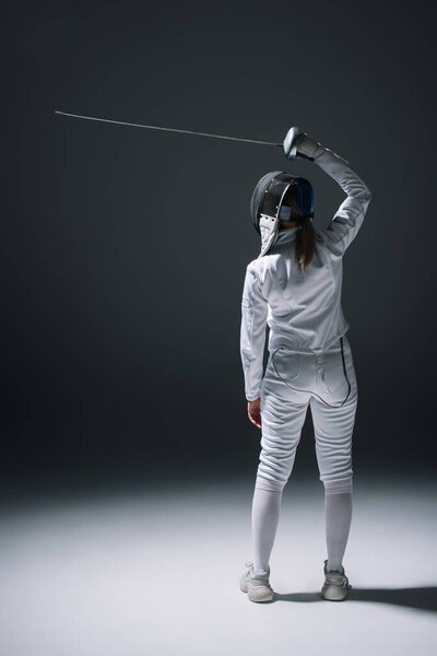Back view of fencer in fencing mask holding rapier on black background