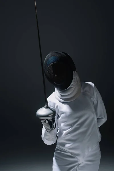Fencer in fencing mask holding rapier isolated on black