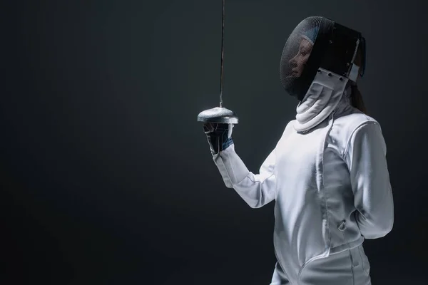 Side view of fencer in fencing mask holding rapier isolated on black