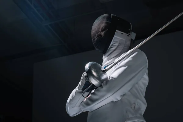 Low angle view of fencer in fencing mask holding rapier
