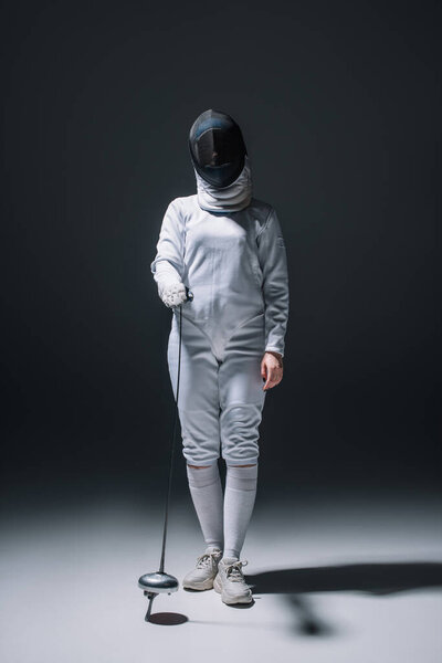 Fencer in fencing mask holding rapier on black background