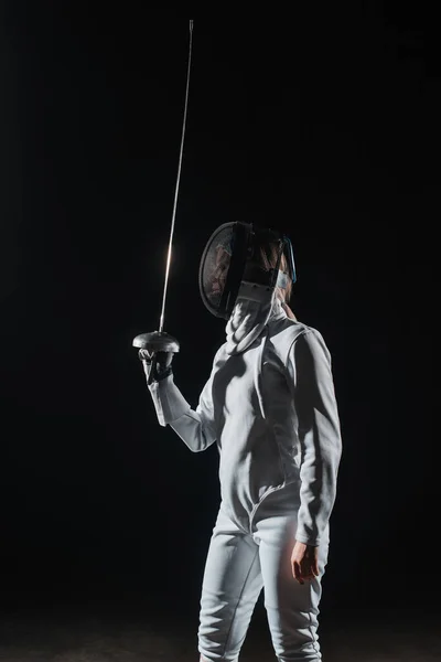 Fencer in fencing mask holding rapier isolated on black