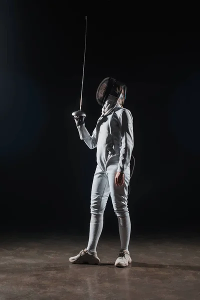 Fencer in fencing mask holding rapier on black background