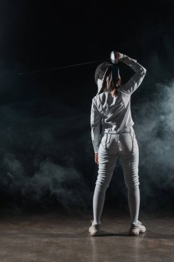 Back view of swordswoman fencing on black background with smoke  clipart