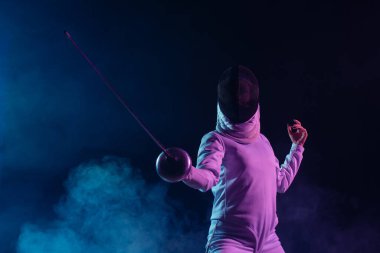 Low angle view of swordswoman fencing on black background with smoke and lighting  clipart