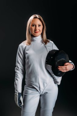 Beautiful fencer looking at camera while holding fencing mask isolated on black  clipart
