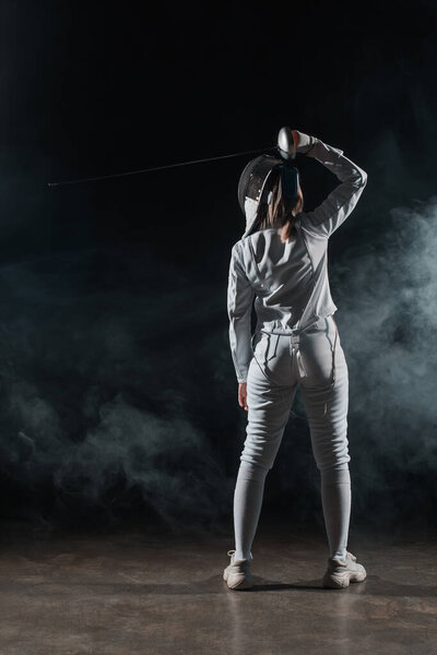 Back view of swordswoman fencing on black background with smoke 