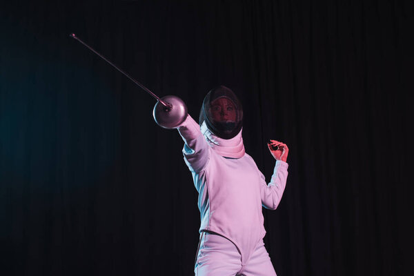 Low angle view of fencer training with rapier isolated on black 