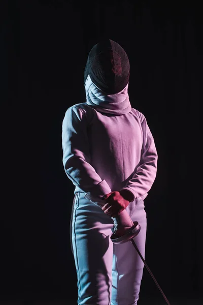 Fencer in fencing mask holding rapier isolated on black