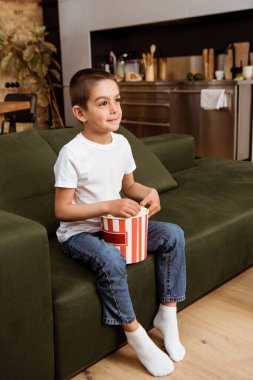 Çocuk kanepede film izlerken elinde patlamış mısır tutuyor. 