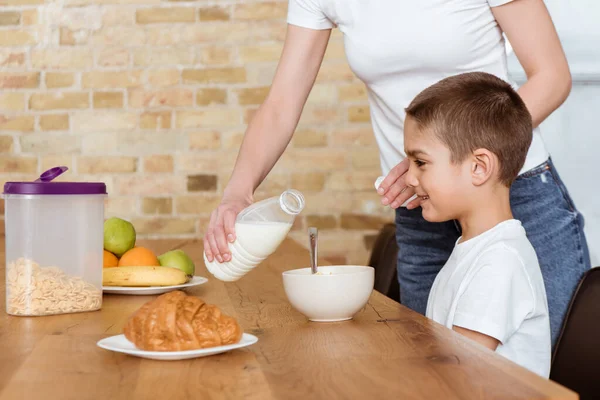 Matka Nalévání Mléka Misce Cereáliemi Blízkosti Usměvavý Syn Kuchyňského Stolu — Stock fotografie