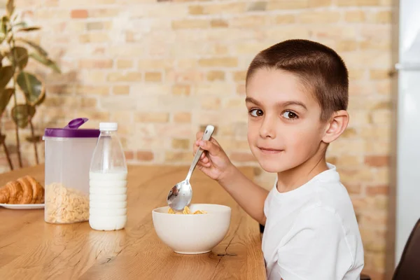 キッチンでシリアルを食べながらカメラを見ている男の子の側面図 — ストック写真