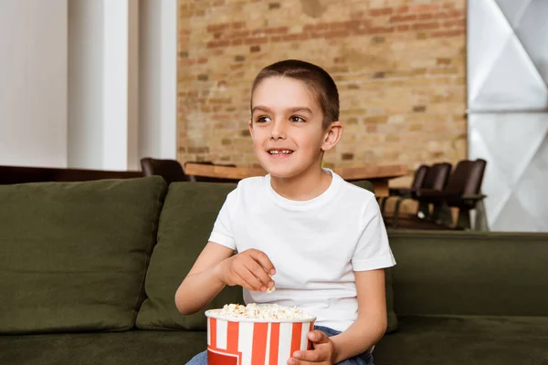 Positiv Pojke Tittar Bort Medan Äter Popcorn Soffan Hemma — Stockfoto