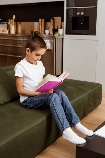 Selective focus of child reading book on couch at home 