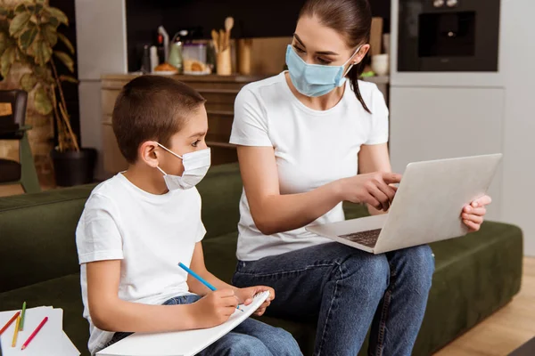 Moeder Medisch Masker Wijzend Naar Laptop Naar Kind Met Kleurpotlood — Stockfoto