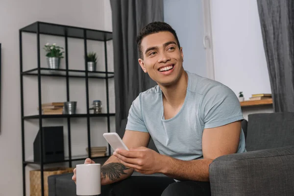 Cheerful Mixed Race Man Tattoo Holding Cup Smartphone — Stock Photo, Image