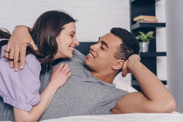 handsome bi-racial man lying on bed and hugging attractive girl 