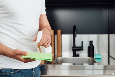 Apartmanı temizlerken elinde bez parçası ve sprey şişesiyle gezen adam manzarası. 