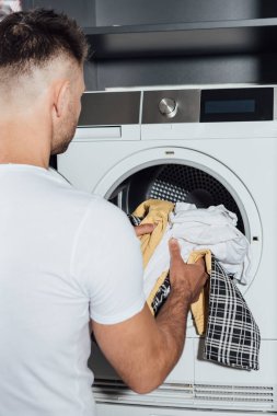 Kirli çamaşırları modern çamaşır makinesine koyan adam. 