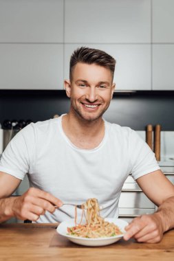 Mutfakta erişte yerken kameraya gülümseyen yakışıklı adamın seçici odağı. 
