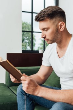 Evdeki kanepede kitap okuyan yakışıklı adamın seçici odağı. 