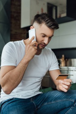 Akıllı telefondan konuşan ve evde kredi kartı tutan adamın seçici odak noktası 