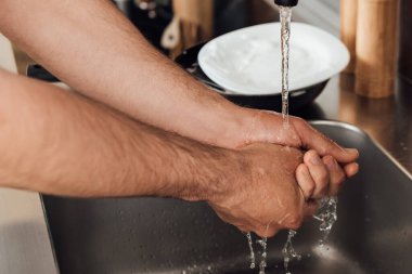 Mutfaktaki çalışma masasının yanında ellerini yıkayan adam görüntüsü. 