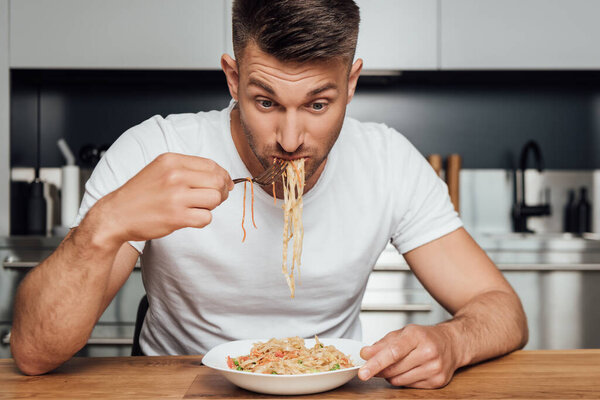 Man eating delicious noodles while sitting at kitchen table 