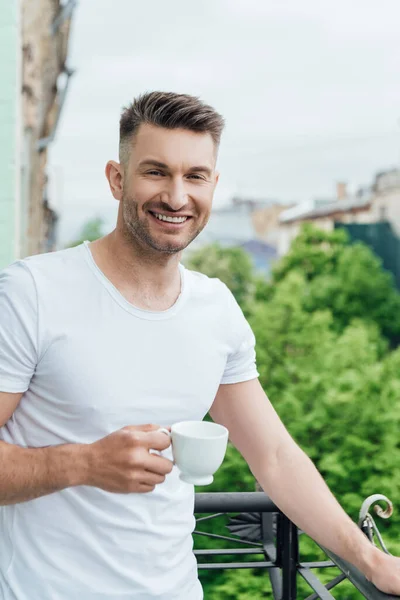 Hombre Guapo Sonriendo Cámara Mientras Sostiene Taza Café Balcón — Foto de Stock