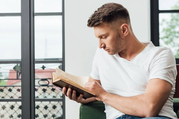 Όμορφος Άνθρωπος Διαβάζει Βιβλίο Στον Καναπέ Κοντά Παράθυρα Στο Σαλόνι — Φωτογραφία Αρχείου