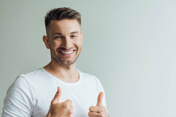 Handsome man smiling at camera and showing thumbs up isolated on grey 