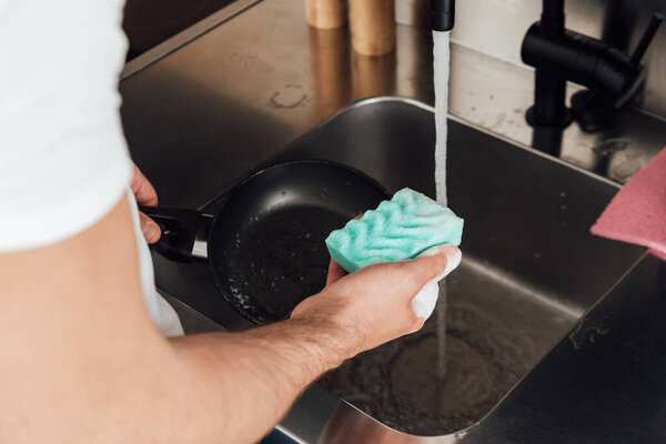 Cropped view of man cleaning frying pan with sponge in kitchen 