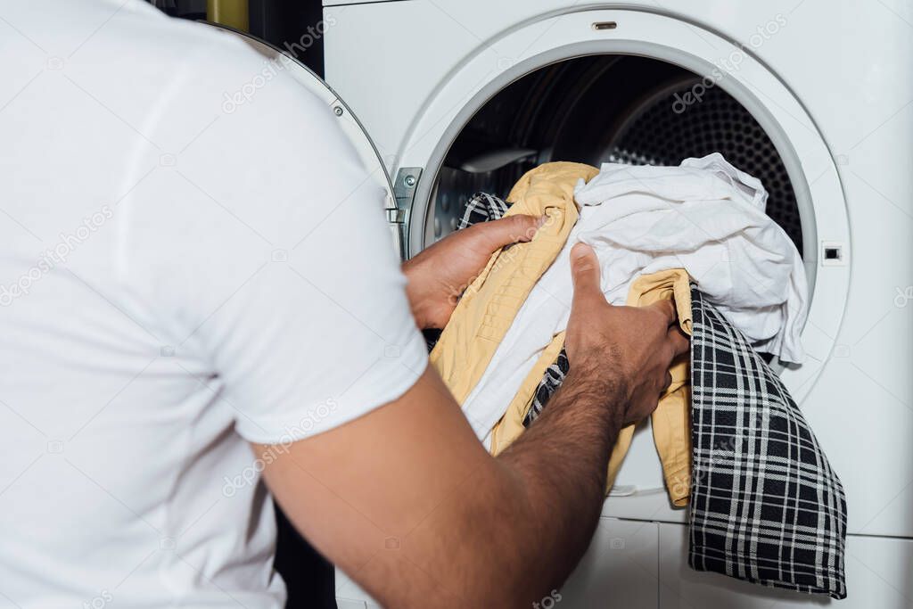 cropped view of man putting dirty laundry in modern washing machine 