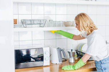 attractive woman in rubber gloves doing housework in kitchen clipart