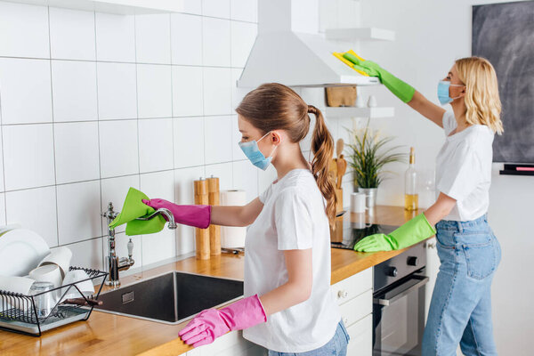 selective focus of sisters in medical masks doing housework in kitchen 