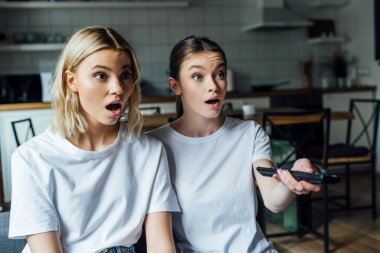 Excited sisters clicking channels on couch at home  clipart