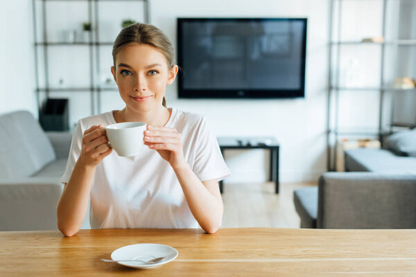 happy woman looking at camera and holding cup of coffee