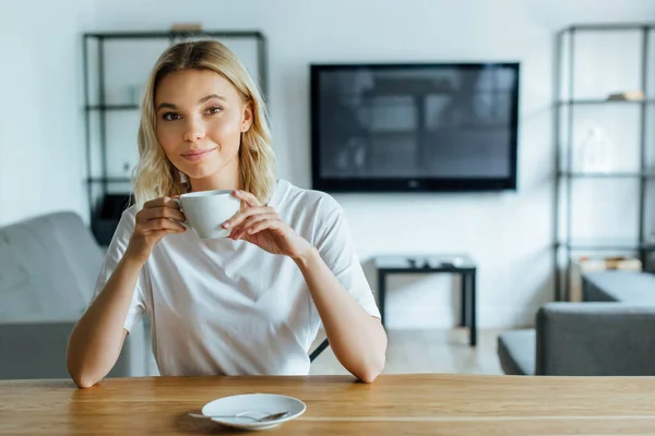 明るい若い女性がカメラを見てコーヒーを飲みながら — ストック写真