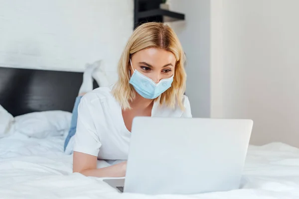 Selective Focus Blonde Woman Medical Mask Using Laptop While Lying — Stock Photo, Image