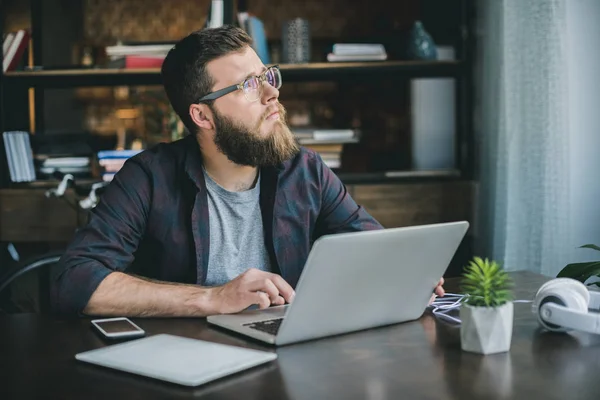 Pensive bearded man typing on laptop — Stock Photo