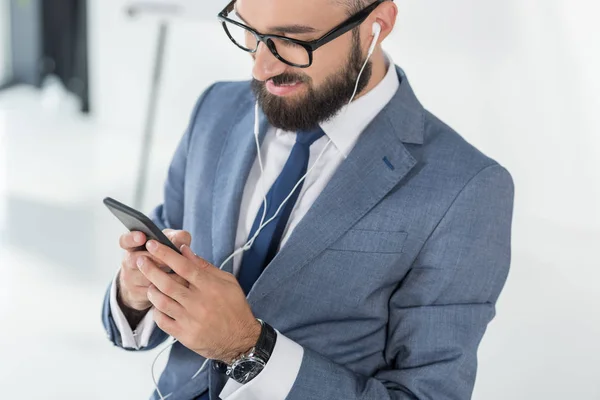 Homem de negócios em fones de ouvido usando smartphone — Fotografia de Stock