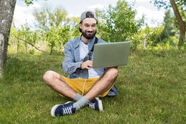 Человек с ноутбуком сидит на траве — стоковое фото