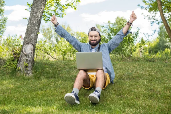 Человек с ноутбуком сидит на траве — стоковое фото