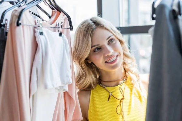 Beautiful blonde woman choosing clothes in store — Stock Photo