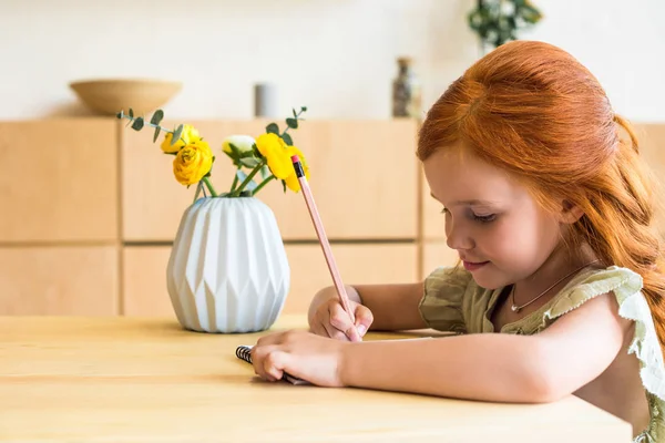 Рыжая девушка рисует за столом — стоковое фото