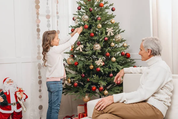 Abuelo y nieta decorando árbol de navidad - foto de stock