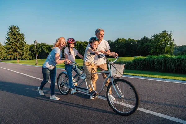 Grands-parents aider les enfants à faire du vélo — Photo de stock