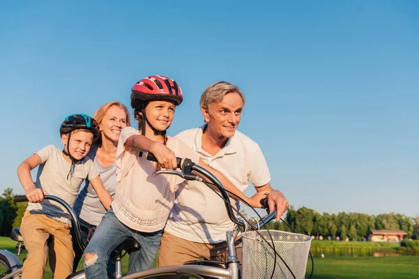Abuelos ayudando a los niños a montar en bicicleta - foto de stock