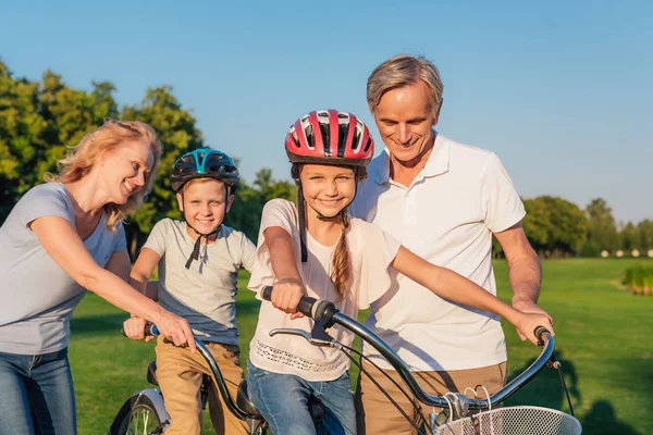 Grandparents helping children ride bicycle — Stock Photo